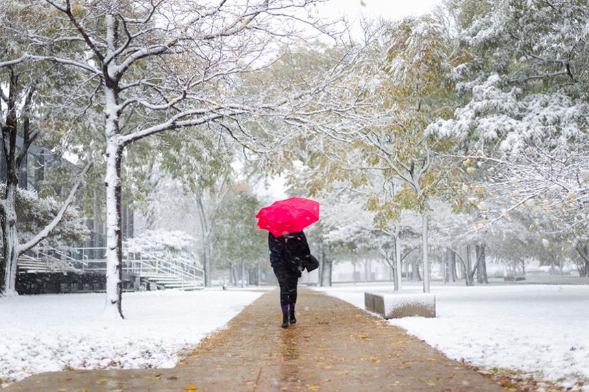 A student walking in the snow on Mies Campus carrying a red umbrella