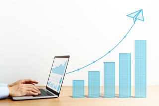 a person typing on a laptop that has a screen of data and marketing analytics. to the right are blue line graphs and arrow pointing up