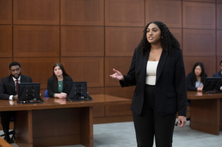 A woman in a black suit stands in a courtroom speaking