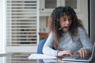 A woman with curly hair fills out a form on a laptop while sitting in a home