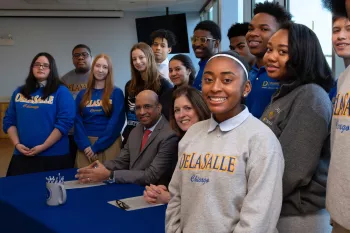 Illinois Tech president Raj Echambadi and De La Salle President Anne Marie Tirpak sign a partnership surrounded by De La Salle students.