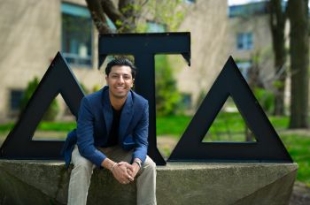 Photo of Shahaan Mirza Mirza (ITM/M.A.S. TENR ’25) sitting in front of the Delta Tau Delta fraternity.
