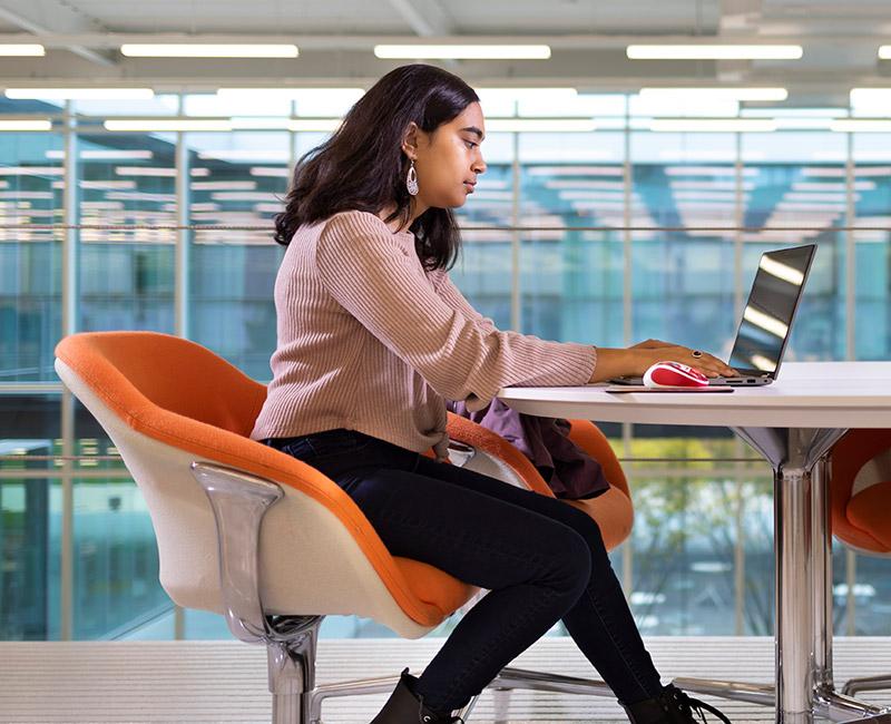 A student sitting inside Kaplan Institute working on a laptop