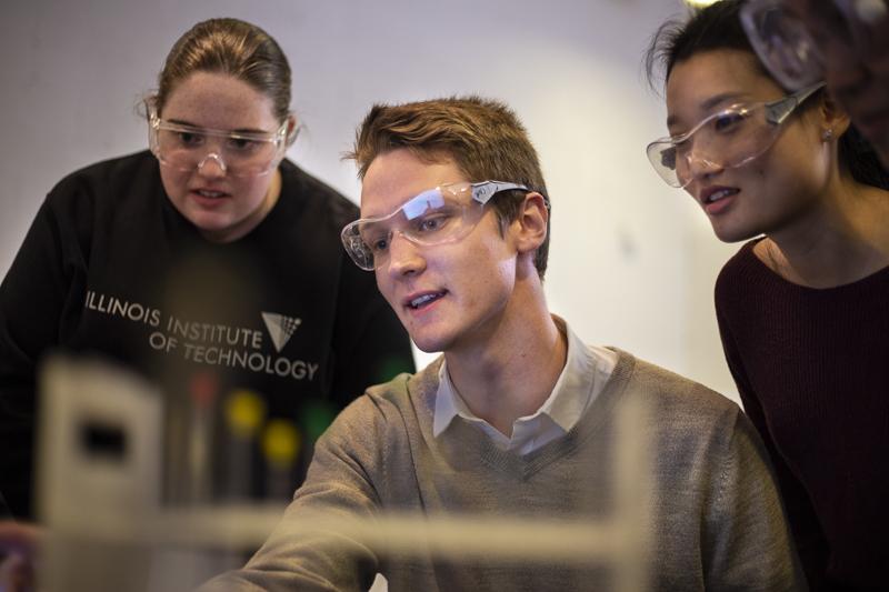 Three students gather around a computer in a chemistry lab