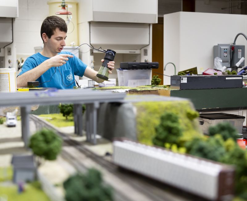 A student in the model railroad association lays grass on a model