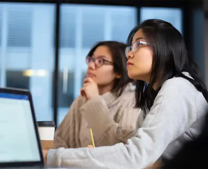 Two students around table with laptop looking up and listening in Stuart Lab